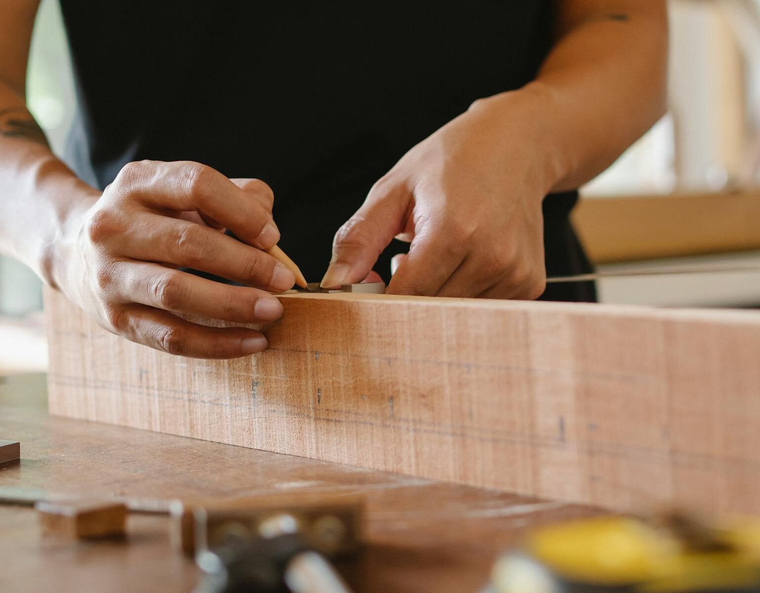 Unrecognizable male master using pencil and ruler to measure width of wooden detail while working in professional workshop on blurred background
